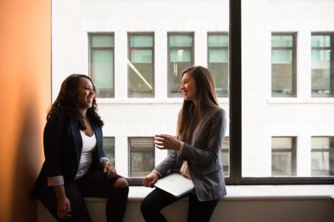 Two colleagues having a conversation whilst sitting on a window ledge