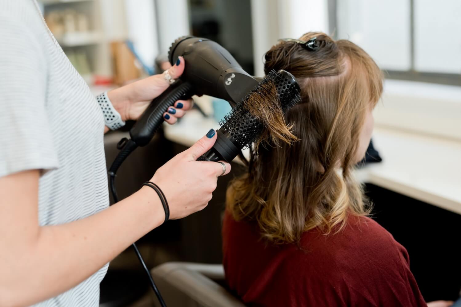 Woman holding hair dryer, drying customers hair.