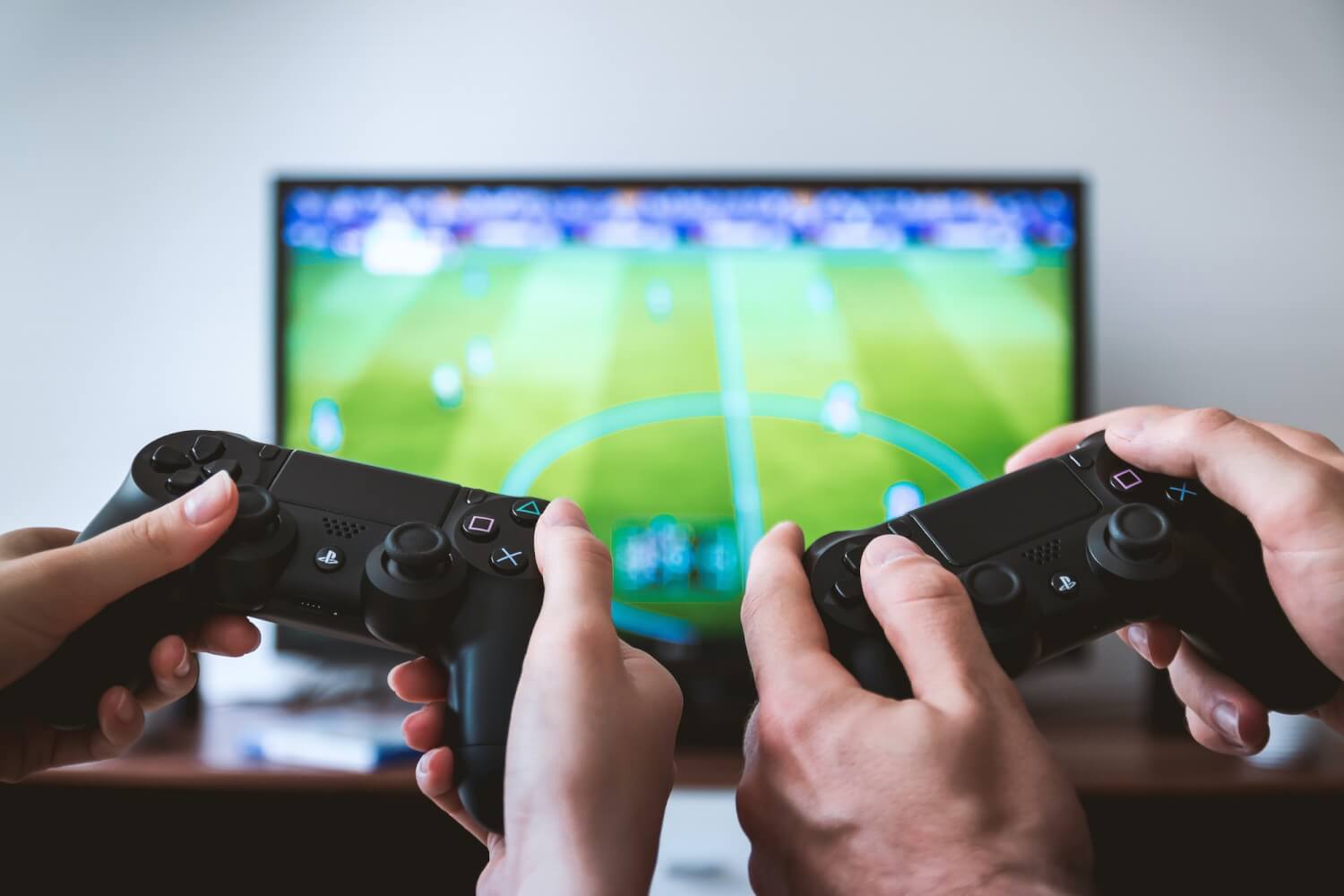 Two hands holding games console controllers in front of a tv screen