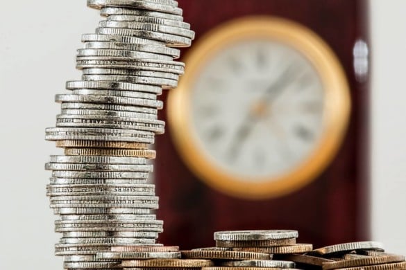 Stack of coins on a table, with a blurred out clock face in the background