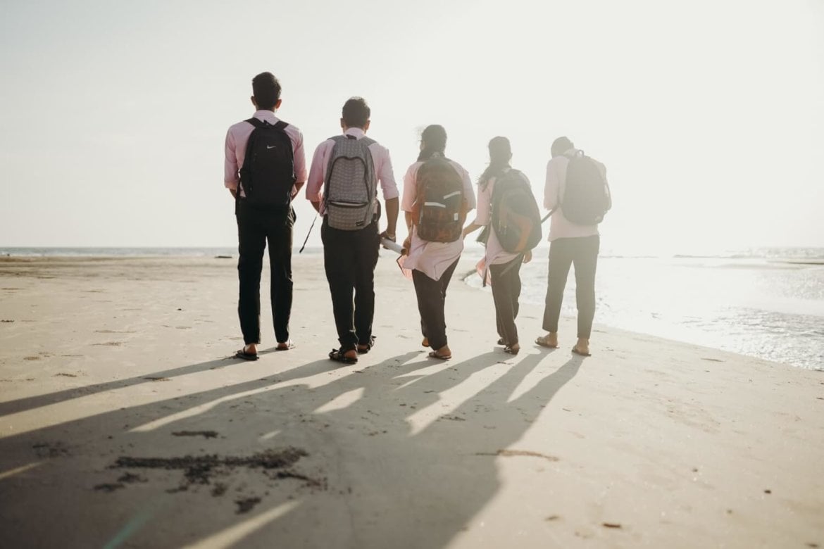 Group of people wearing backpacks and walking on a beach