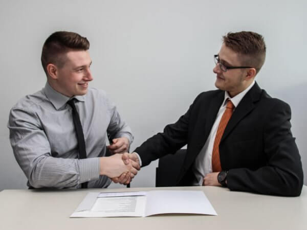 Two people sitting at desk shaking hands