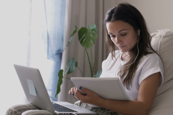 Woman sitting with laptop reading from a notepad