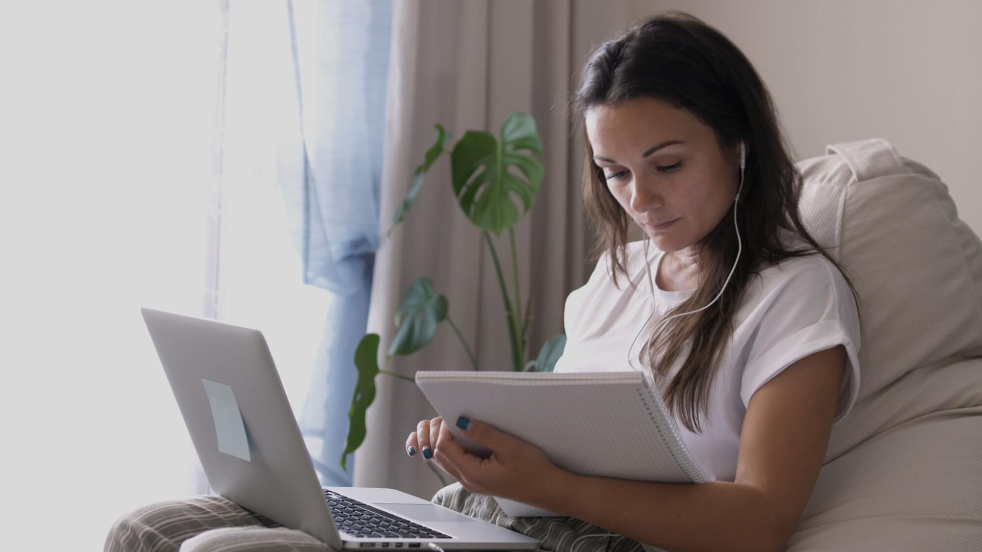 Woman sitting with laptop reading from a notepad