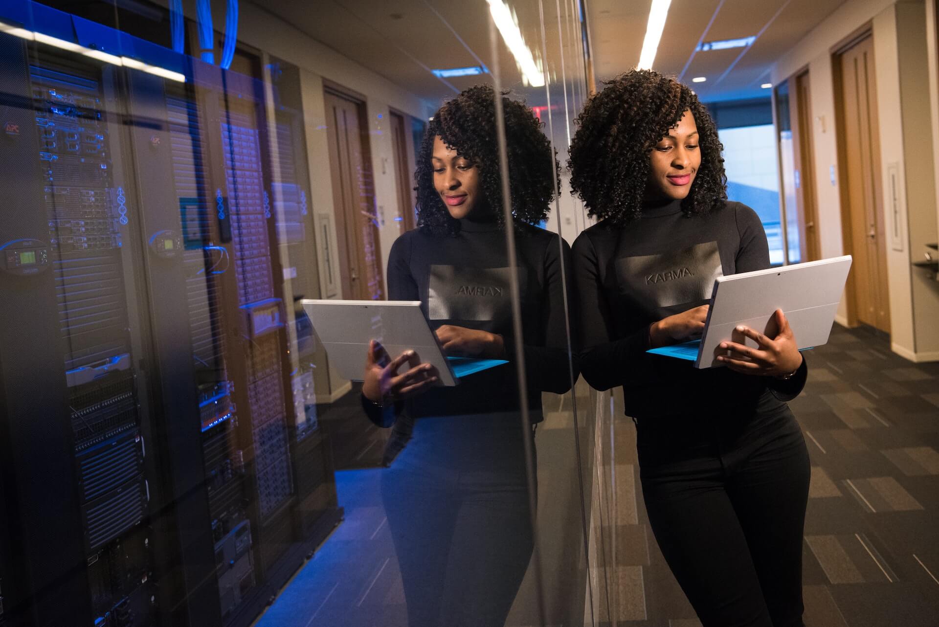 Woman holding laptop next to server room