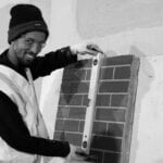 Male construction worker wearing high visibility vest holding spirit level to wall