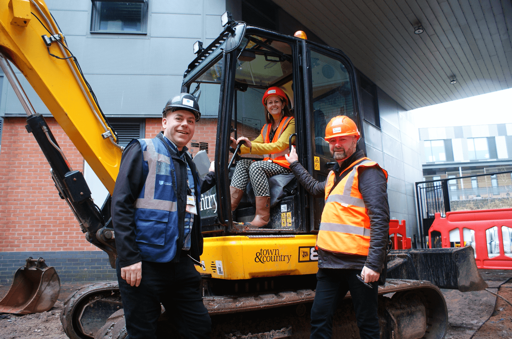 Coventry College Principal and CEO Carol Thomas sitting inside JCB Excavator with 2 construction works standing outside