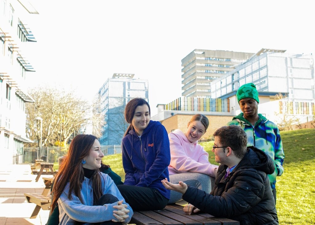 students sitting on bench on coventry college campus