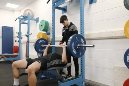 Person in a gym bench pressing with person spotting them